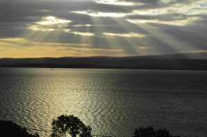 Sun breaking through grey sky over the sea at dusk